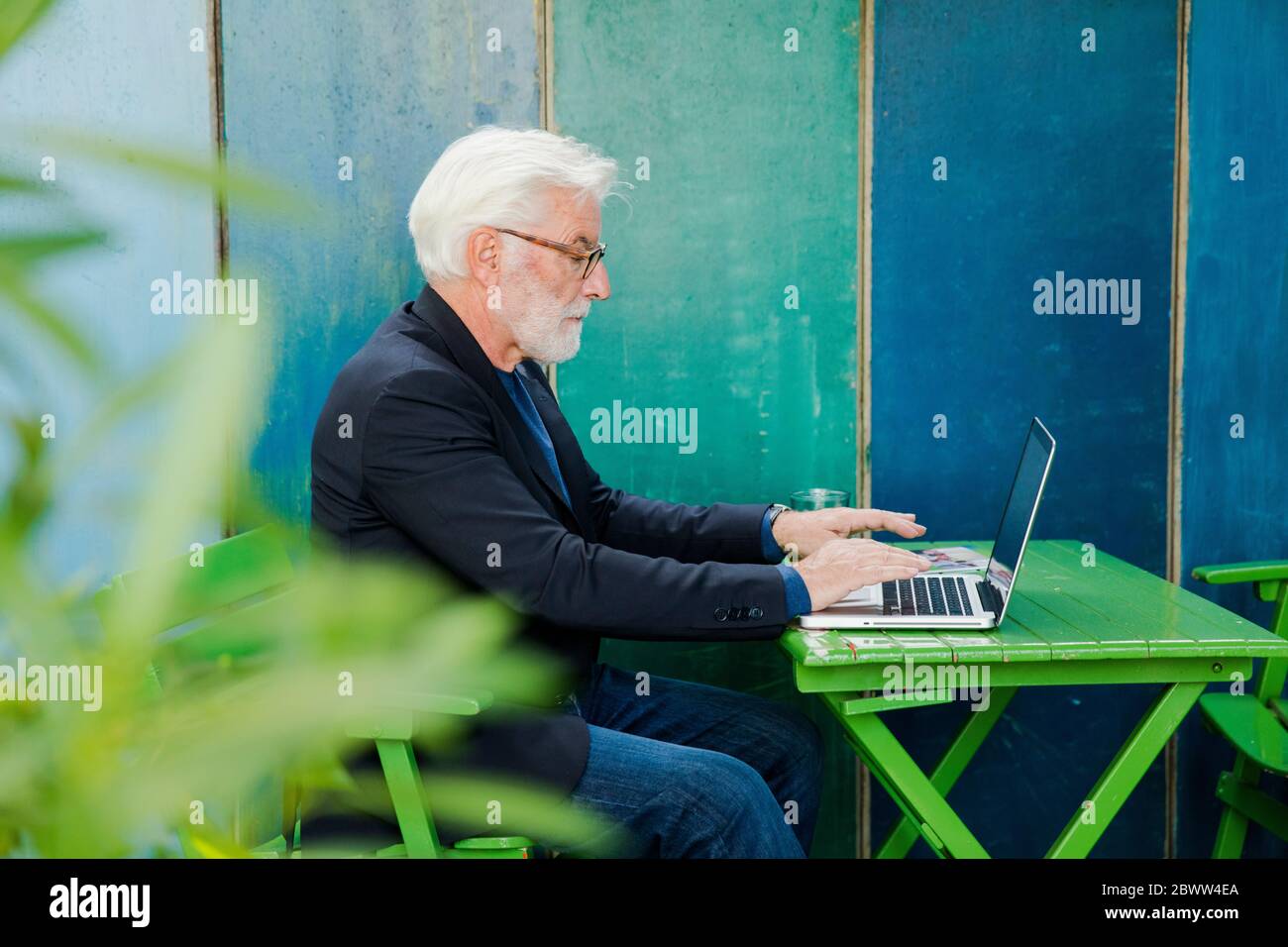 Senior man sitting at table outdoors using laptop Stock Photo