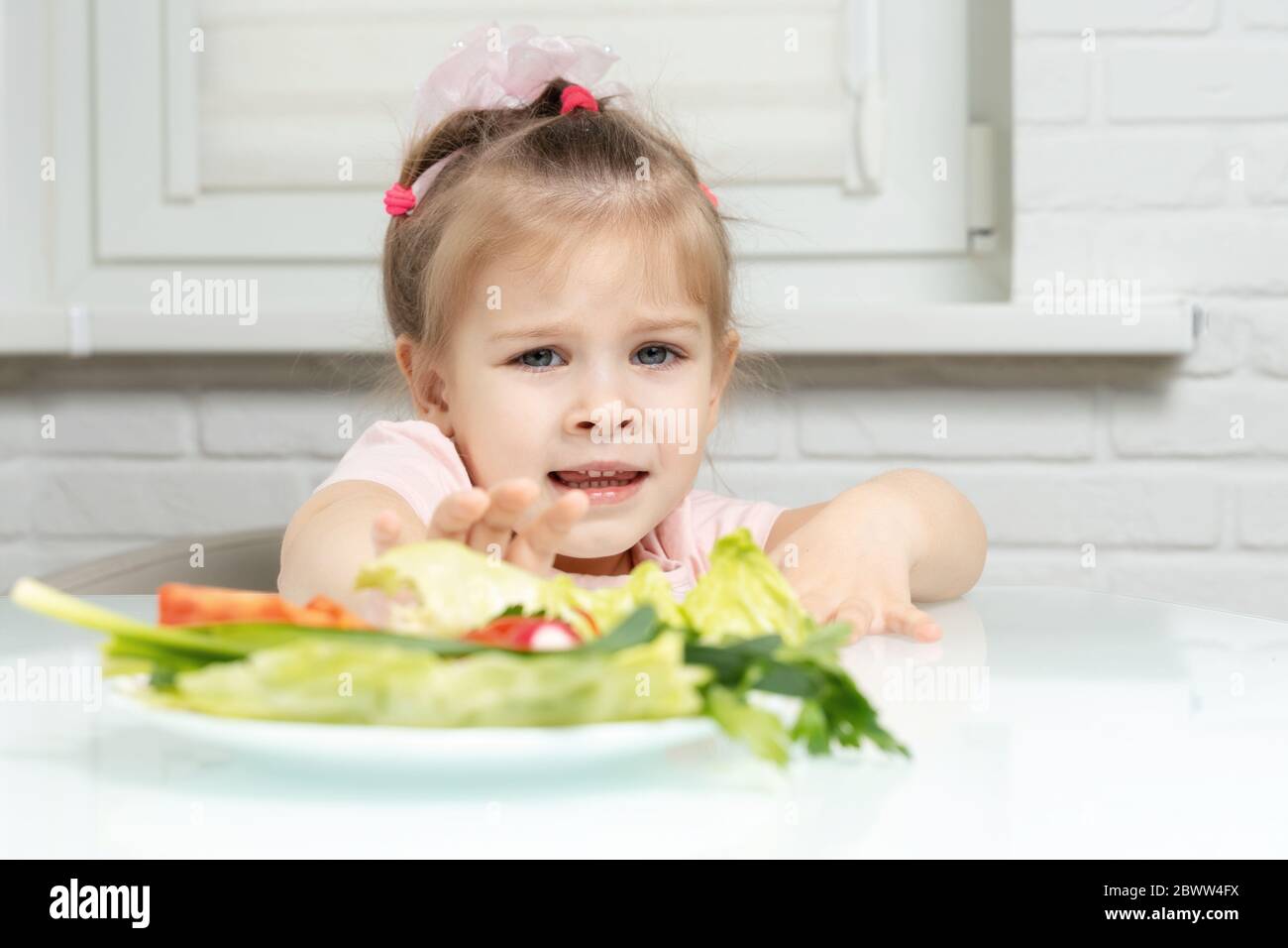 a girl 3 years emotionally repels a plate of vegetables from herself. lack of fruits and vegetables in children's diets Stock Photo