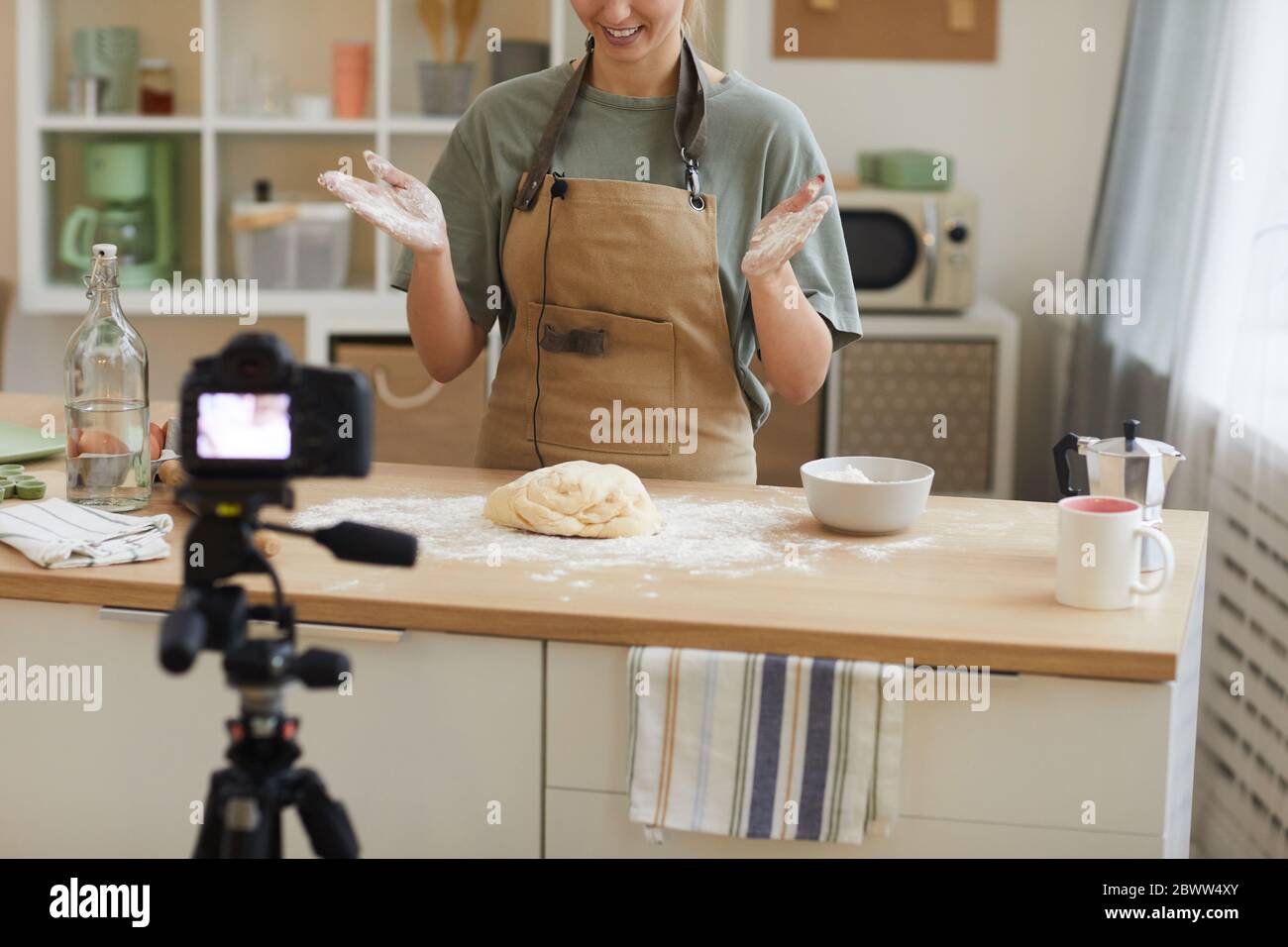Young woman wearing apron standing at the kitchen and making dough for cake and shooting the video for content Stock Photo