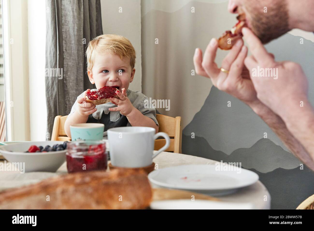 Portrait of little boy eating bread with jam watching his father Stock Photo