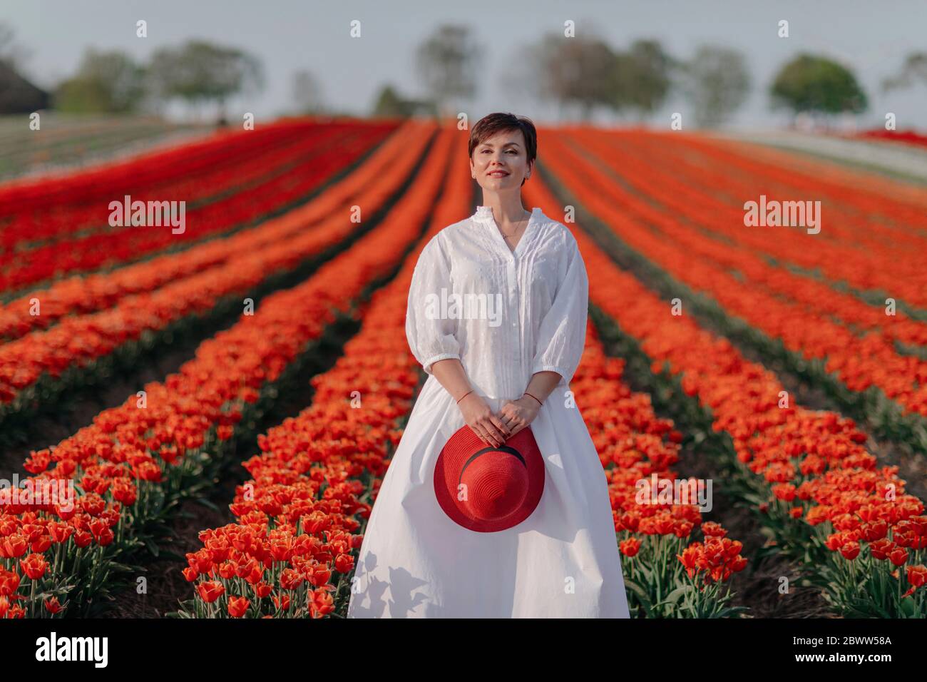 Portrait of smiling woman dressed in white standing in front of tulip field Stock Photo