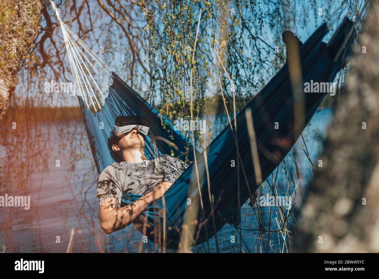 Young man relaxing in hammock, using VR glasses Stock Photo