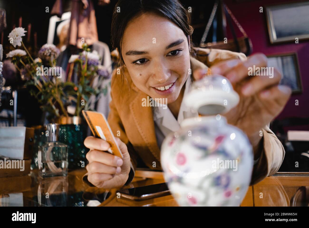 Curious woman with credit card looking at vase in thrift store Stock