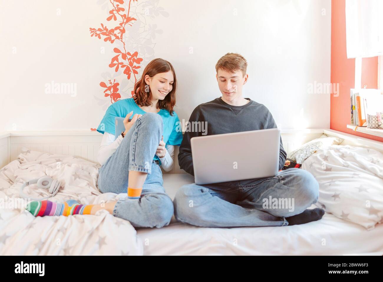 Portrait of teenage couple sitting together on bed learning with laptop Stock Photo