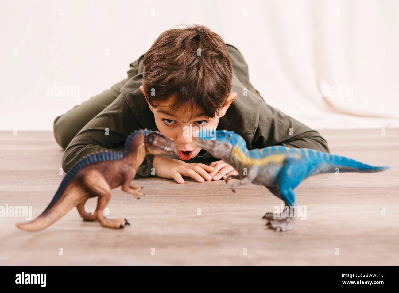 Portrait of little boy crouching on the floor playing with toy dinosaurs Stock Photo