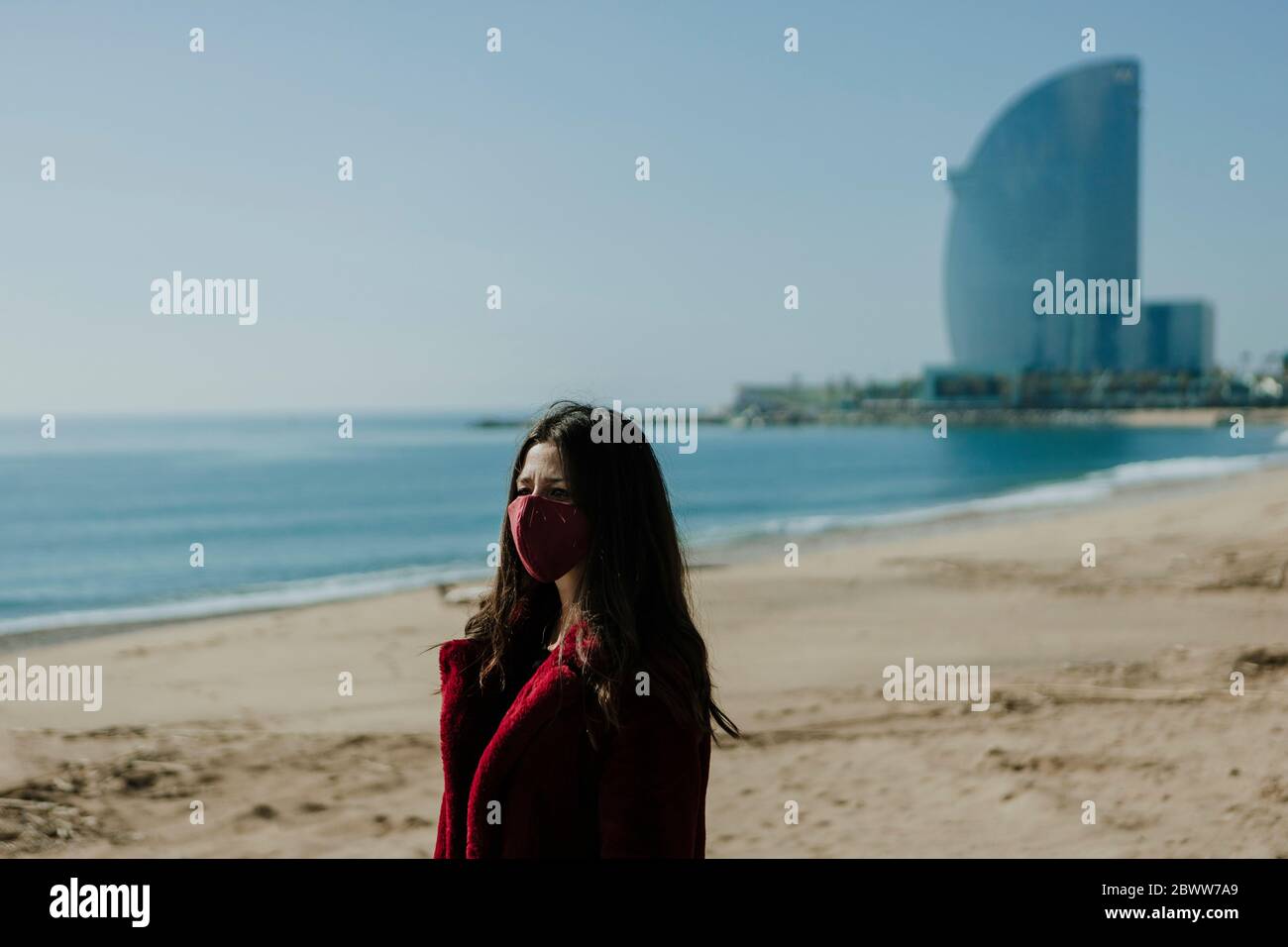 Woman wearing face mask standing at beach against clear sky on sunny day Stock Photo