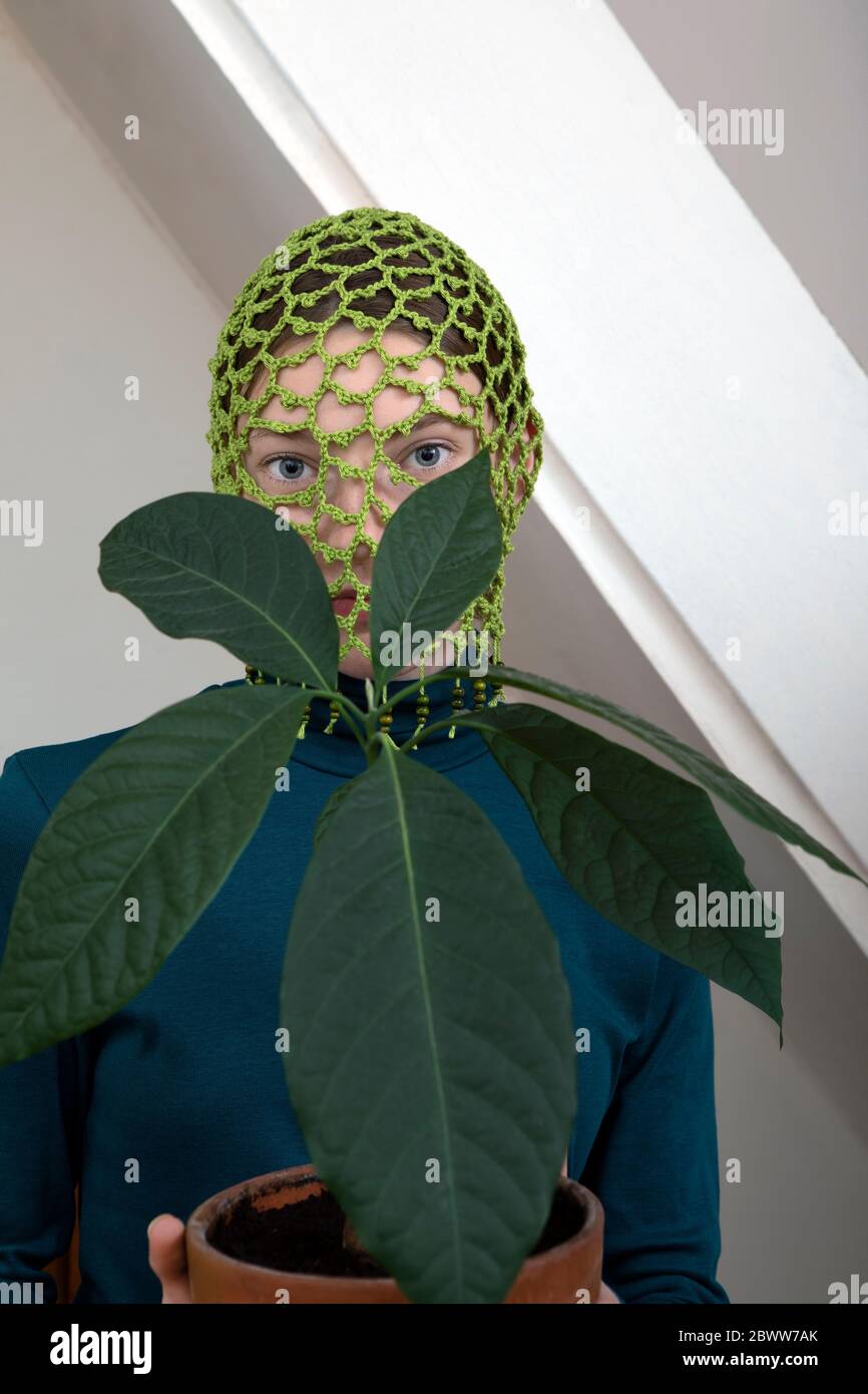 Portrait of teenage girl with potted avocado plant wearing crocheted green headdress Stock Photo