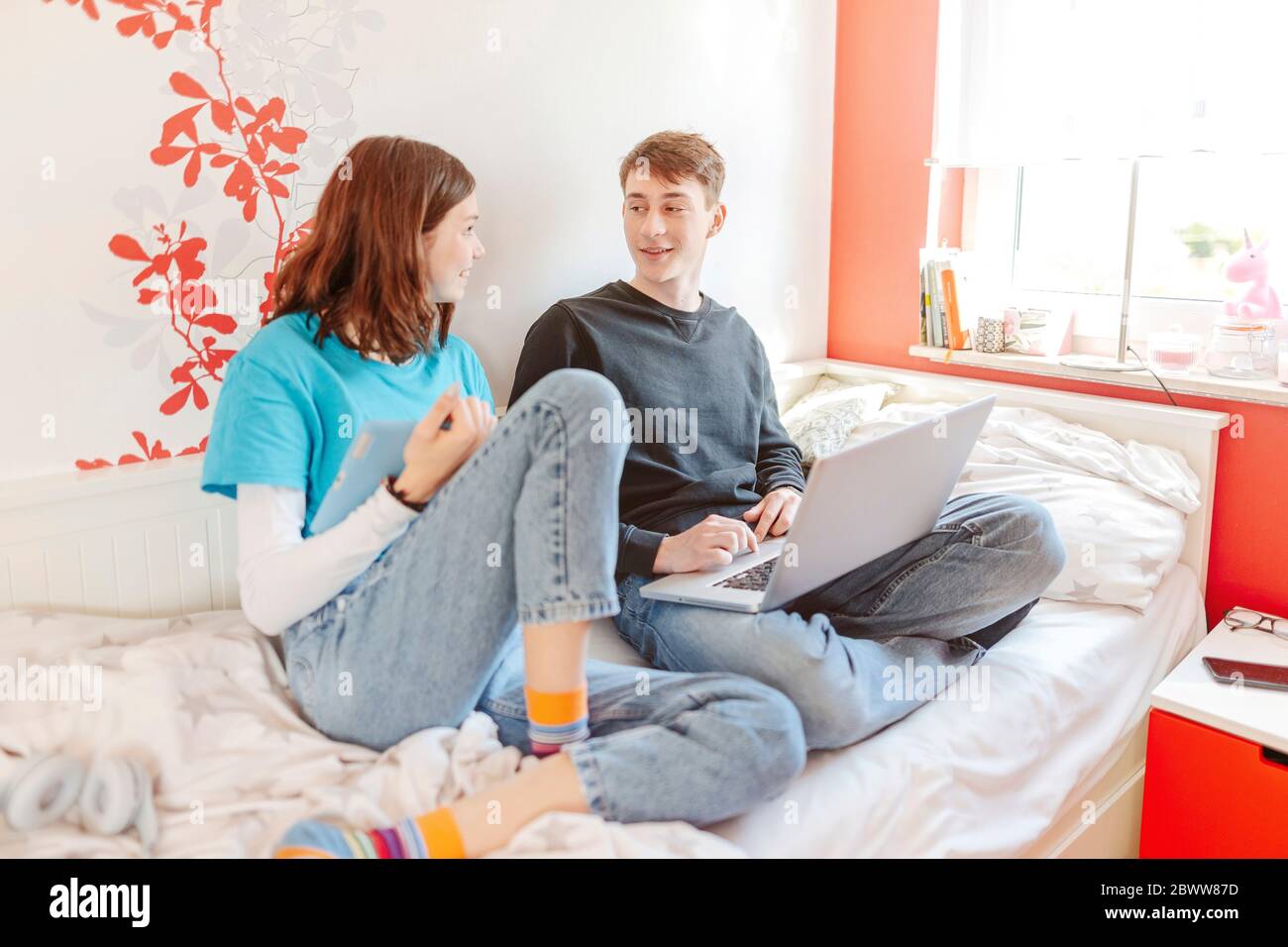 Teenage couple sitting on bed with laptop and digital tablet Stock Photo