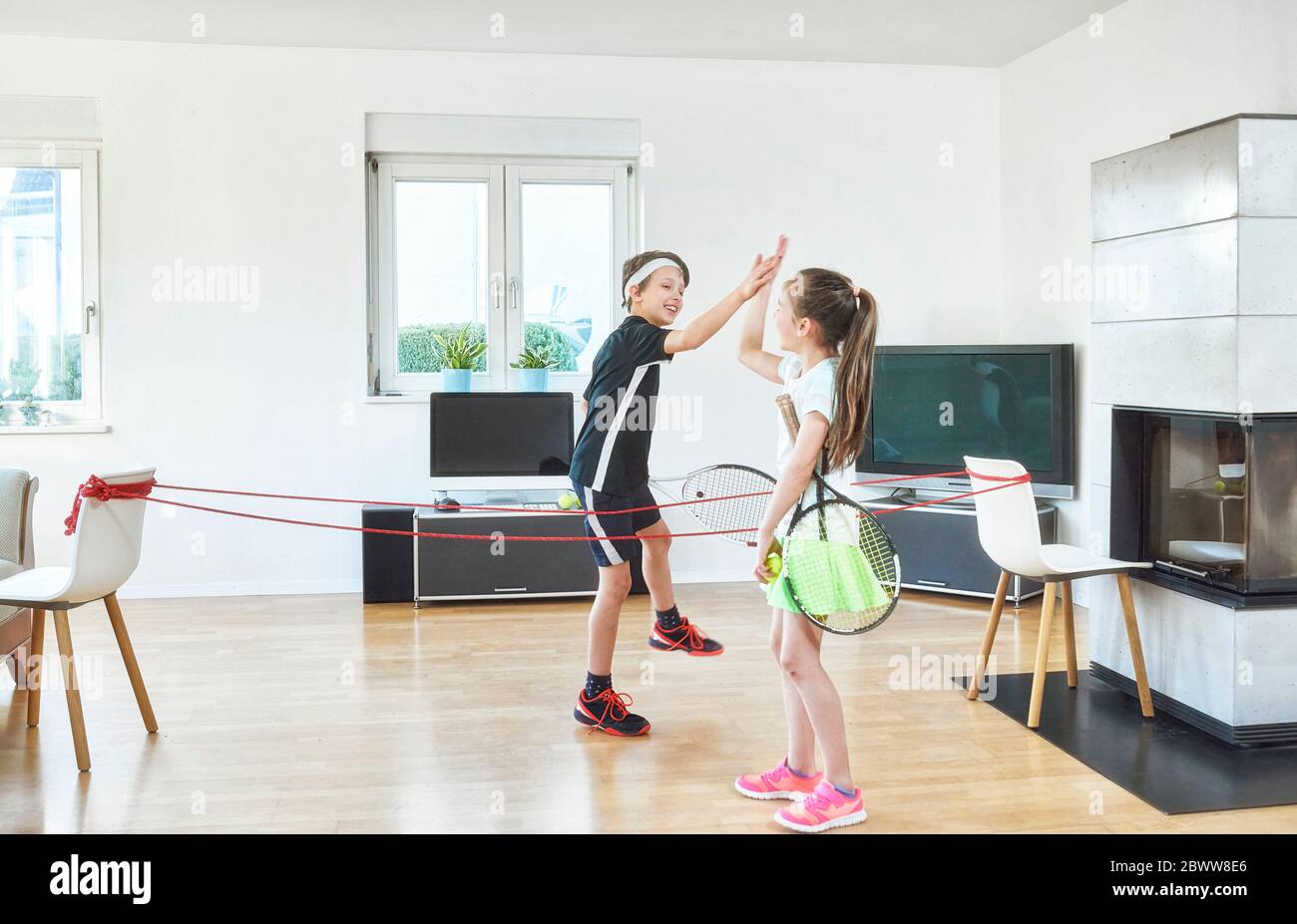 Happy siblings giving high-five while playing tennis at home during pandemic situation Stock Photo