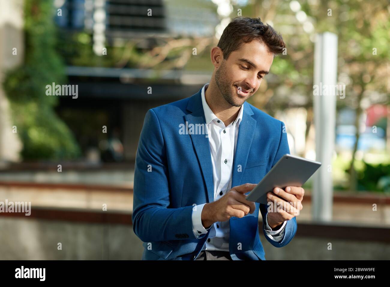 Smiling young businessman standing outside using a digital tablet Stock Photo