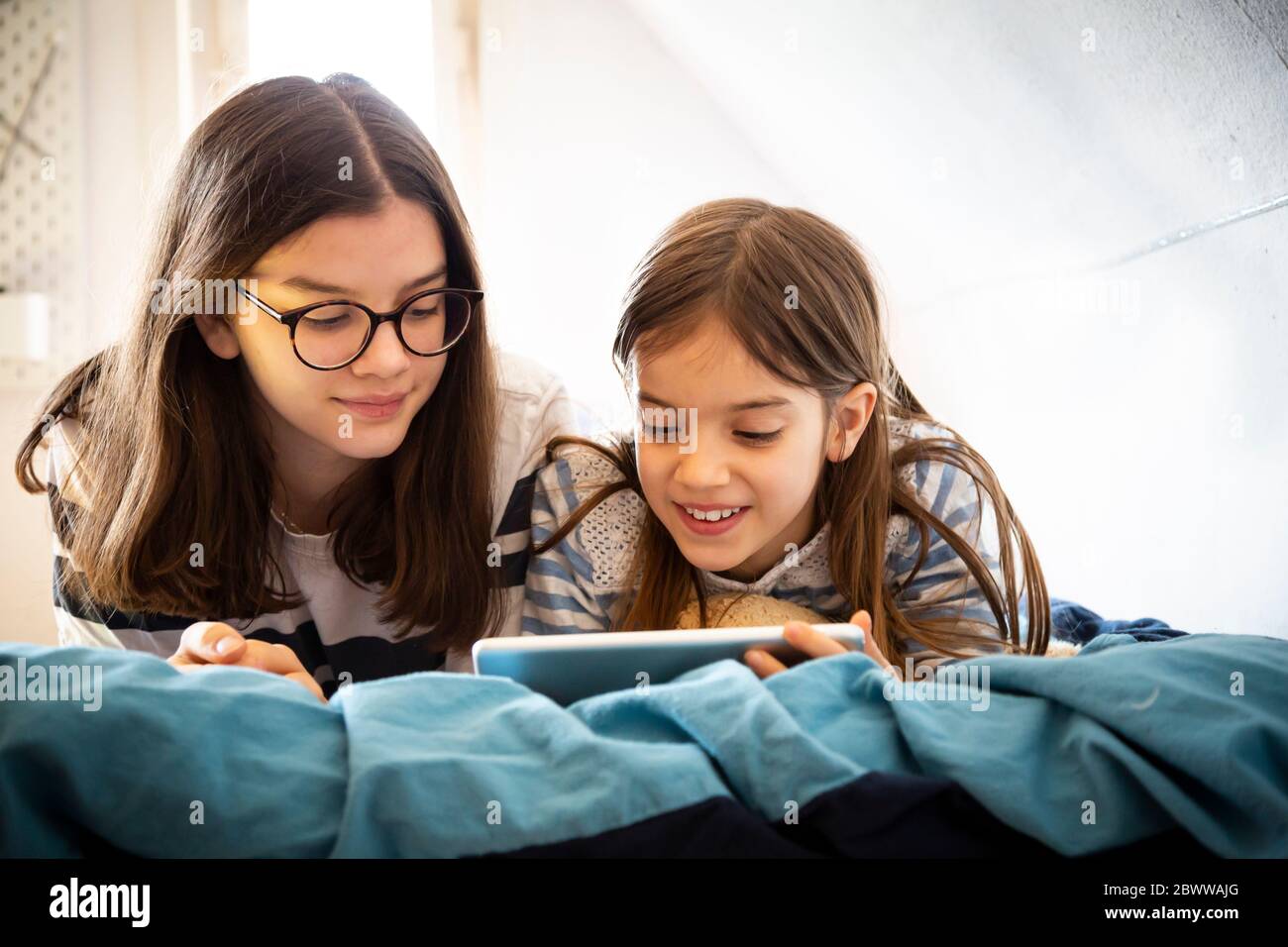 Sisters using tablet lying on bed Stock Photo
