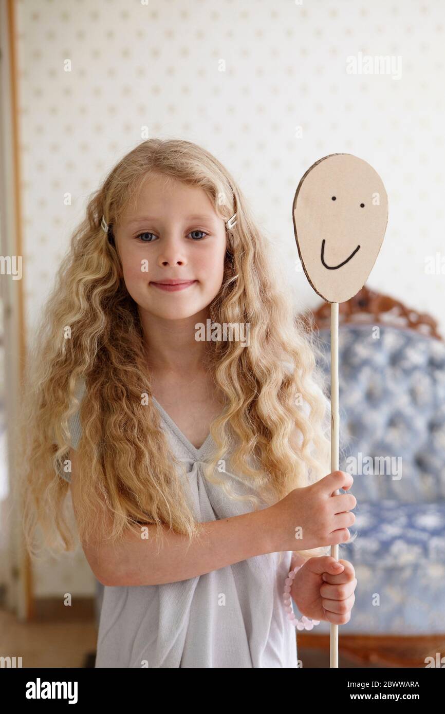 Portrait of a girl holding cardboard smiley face on a stick Stock Photo