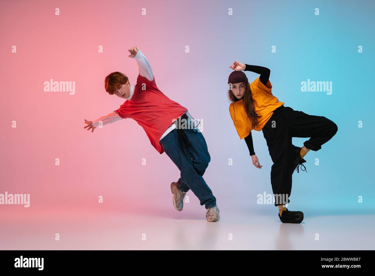 Boy and girl dancing hip-hop in stylish clothes on colorful gradient background at dance hall in neon. Youth culture, movement, style and fashion, action. Fashionable bright portrait. Street dance. Stock Photo