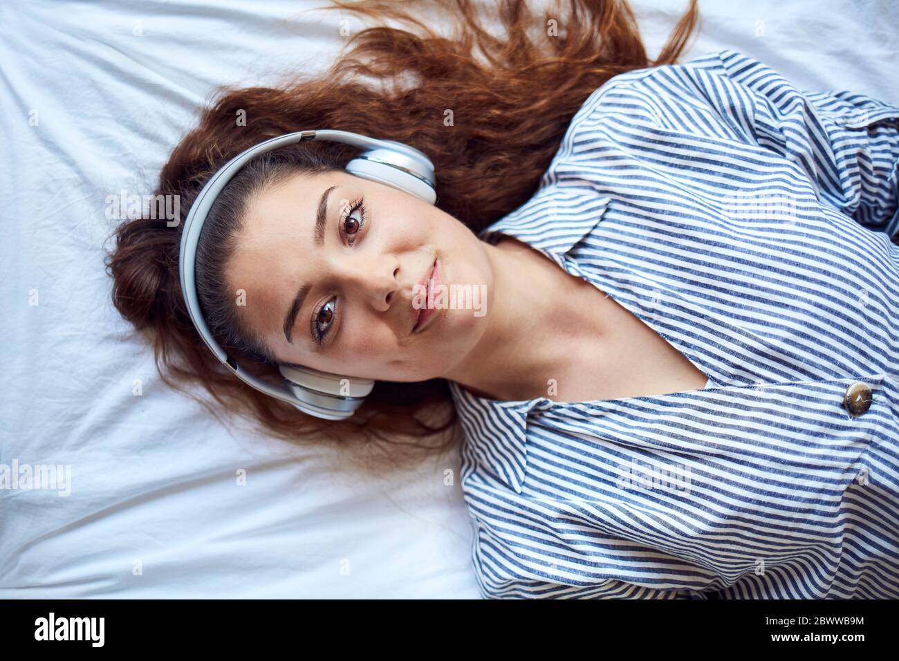 Portrait of smiling young woman lying on bed listening music with ...