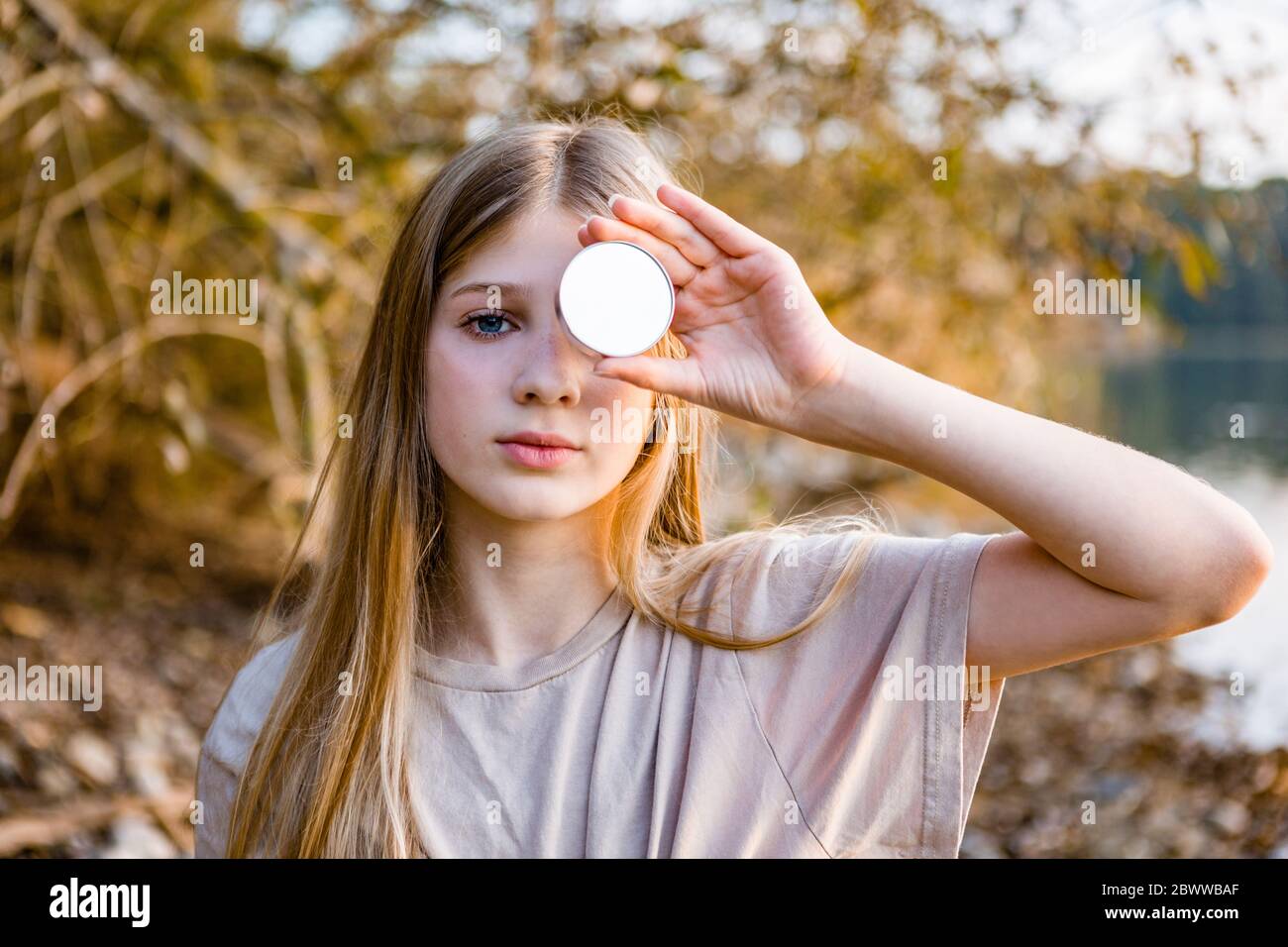 Portrait of girl holding mirror in front of eye during sunset Stock Photo