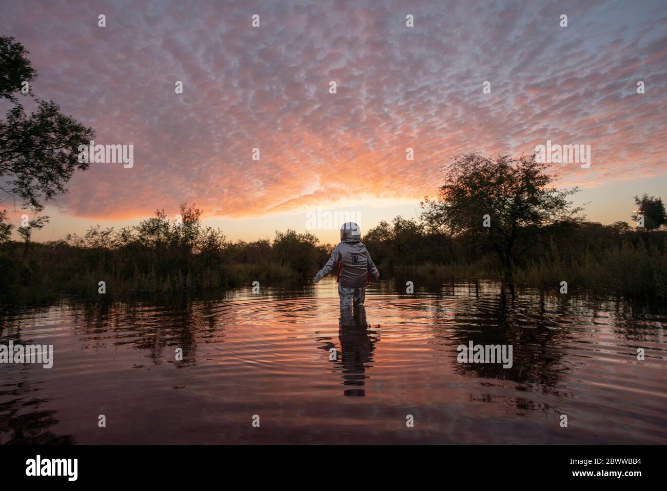 Spacewoman walking in water at sunset Stock Photo