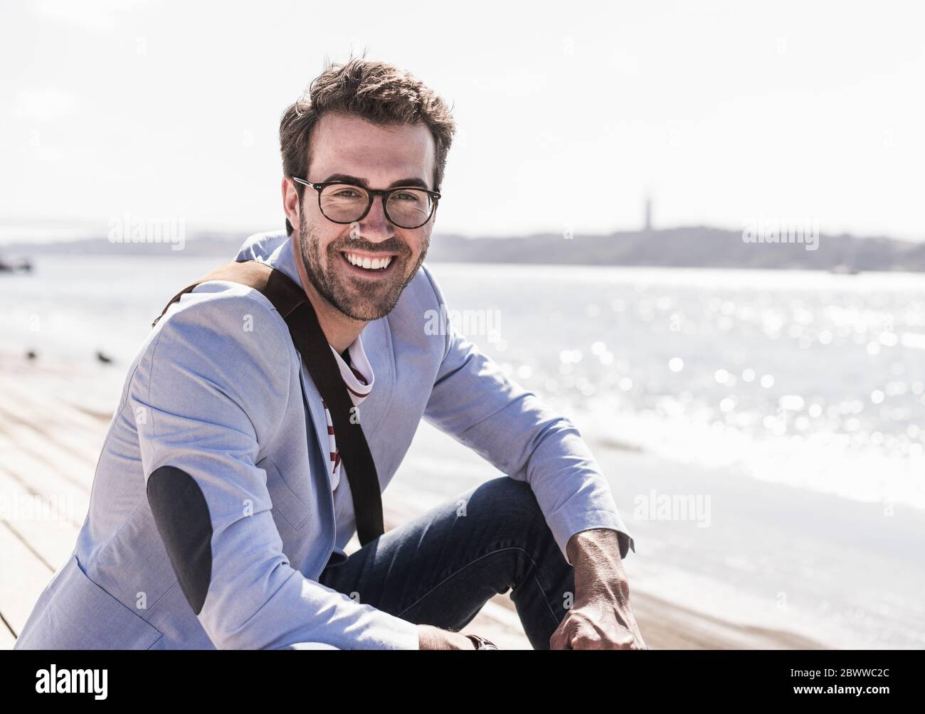 Portrait of happy young man sitting on the waterfront Stock Photo