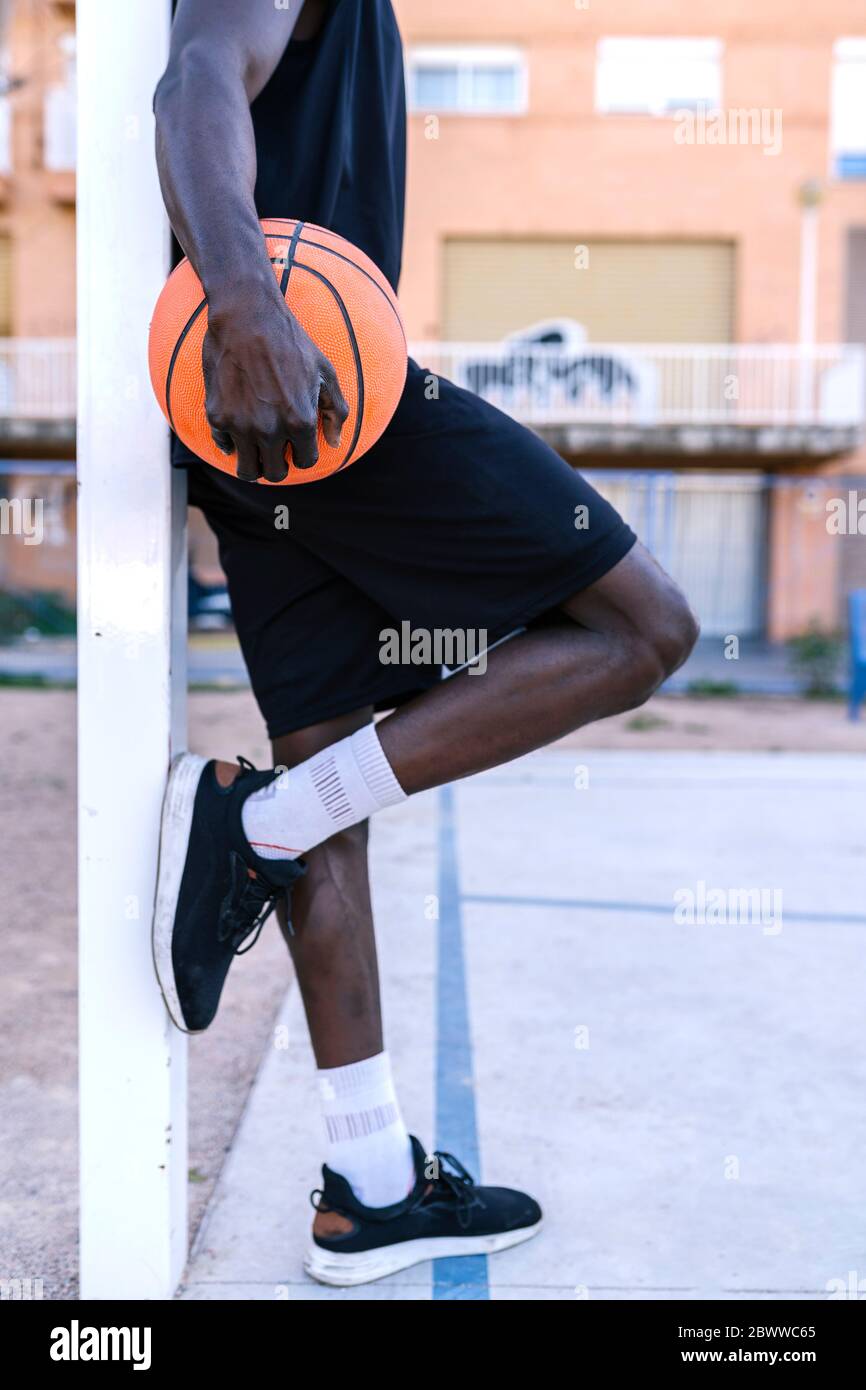 Young man holding basketball leaning on pole on basketball court Stock