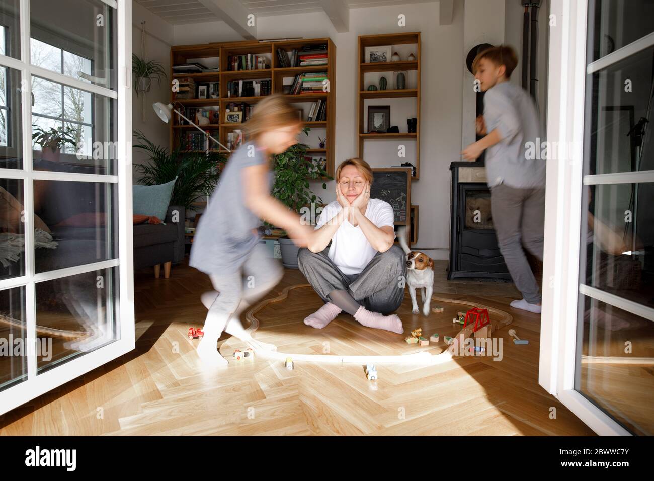 Stressed out mother sitting in the middle of toys, while children are running around her Stock Photo