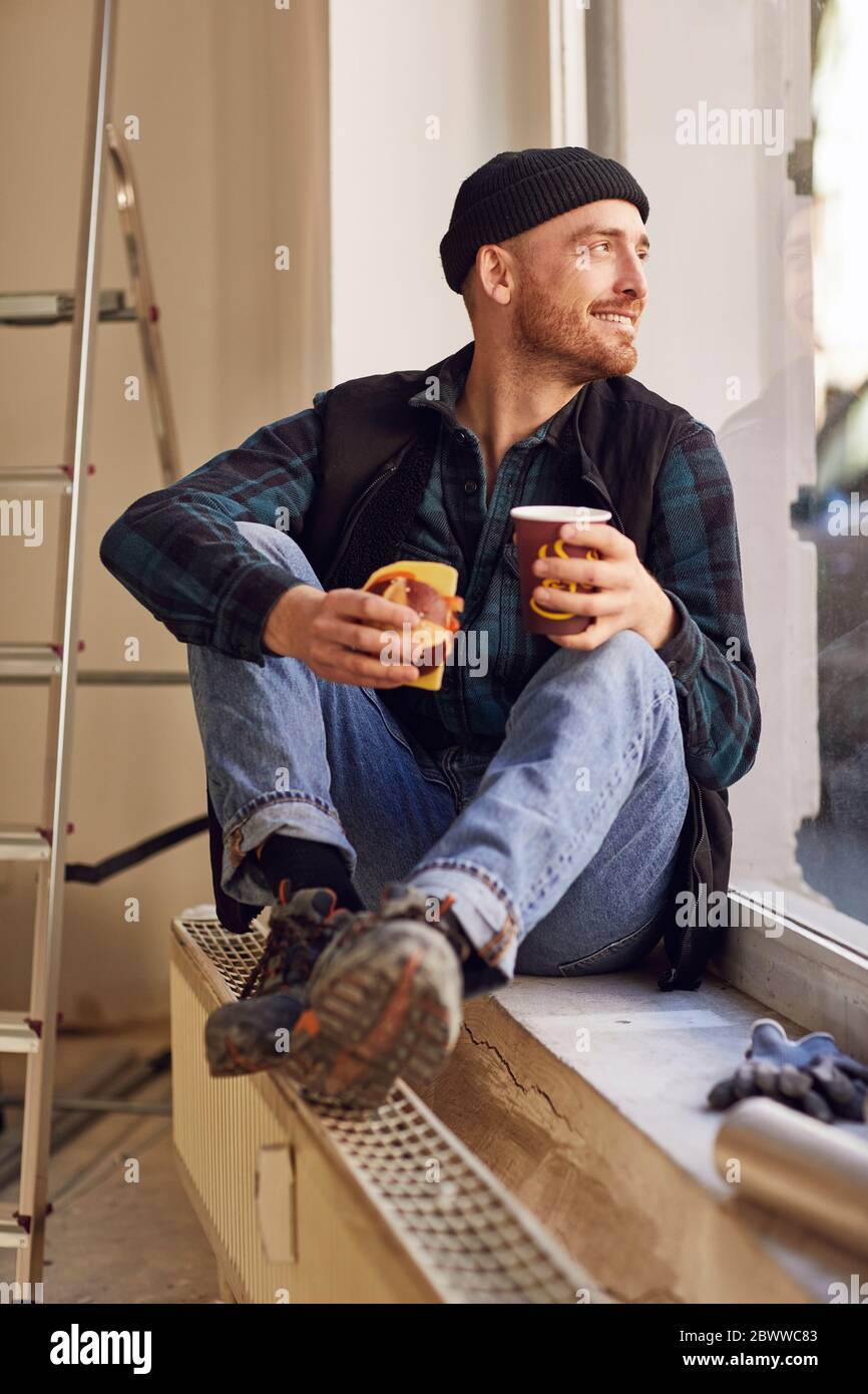 Man refurbishing shop location, sitting on windowsill, drinking coffee Stock Photo
