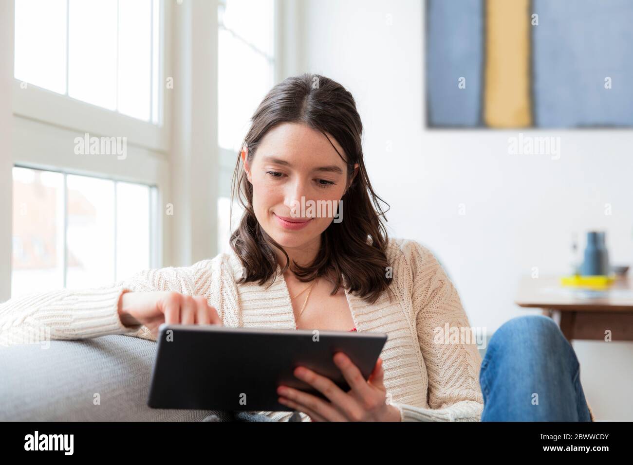 Woman sitting on couch at home using tablet Stock Photo - Alamy