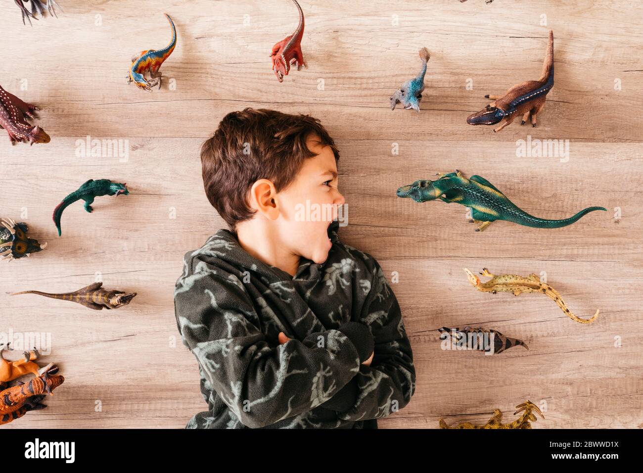 Little boy lying on the floor between toy dinosaurs Stock Photo