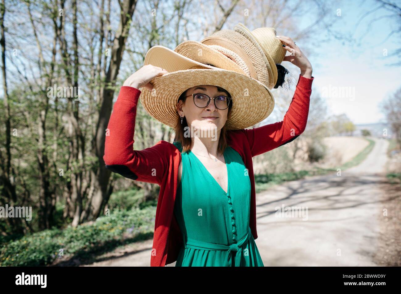 Portrait of mature woman with stack of straw hats on her head outdoors Stock Photo