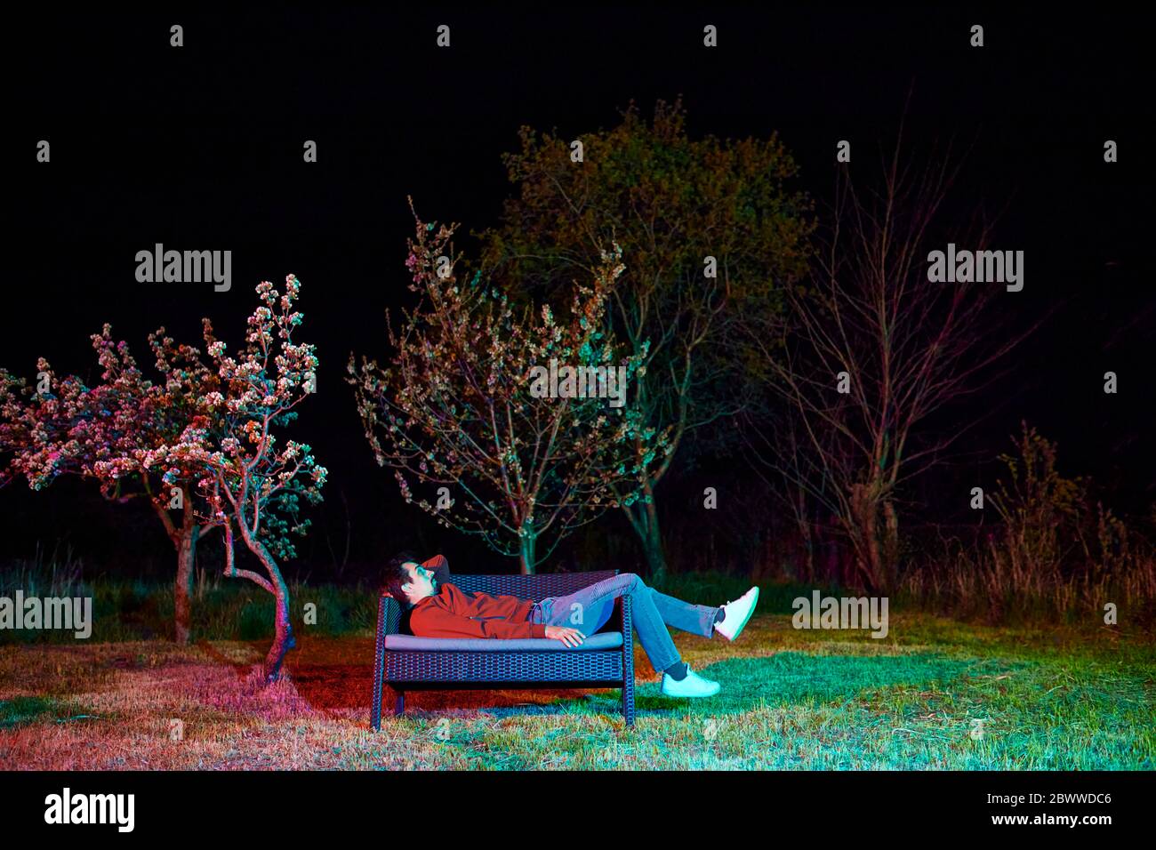 Sad man sitting alone on garden bench at night Stock Photo - Alamy