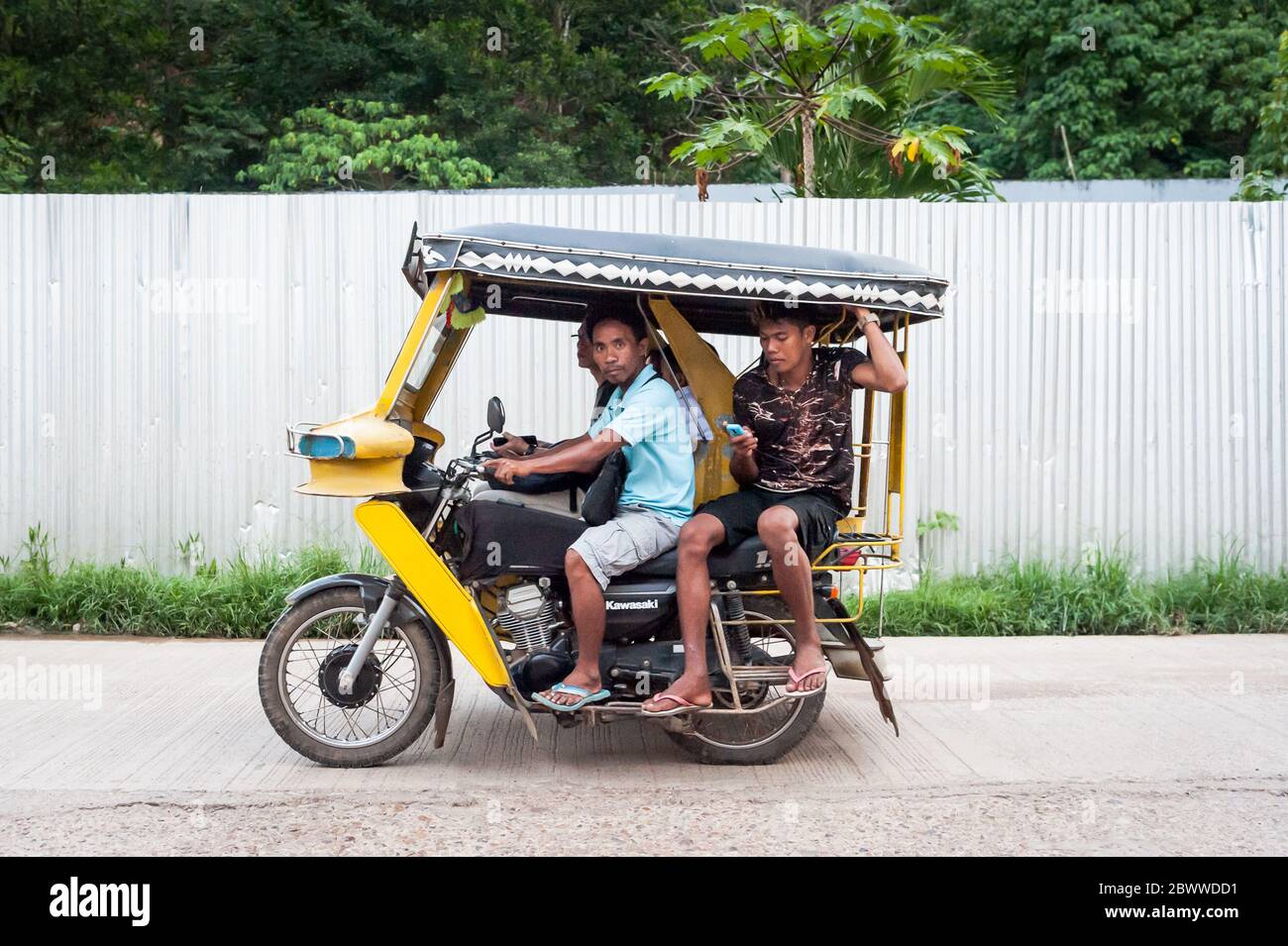 The famous filipino tricycle or tuk tuk (sometimes called rickshaw) makes its way along the busy main road going into Coron Town Proper. Coron Island. Stock Photo