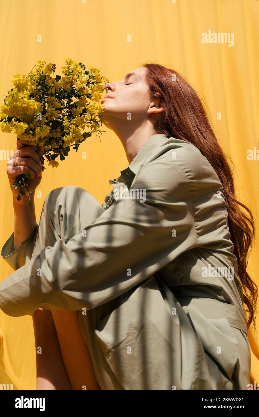 Portrait of redheaded woman with eyes closed holding bunch of yellow ...