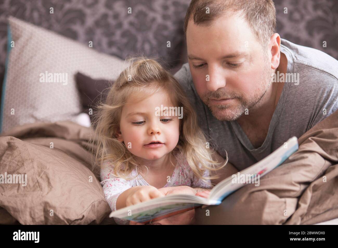 Father and daughter reading a book in bed Stock Photo