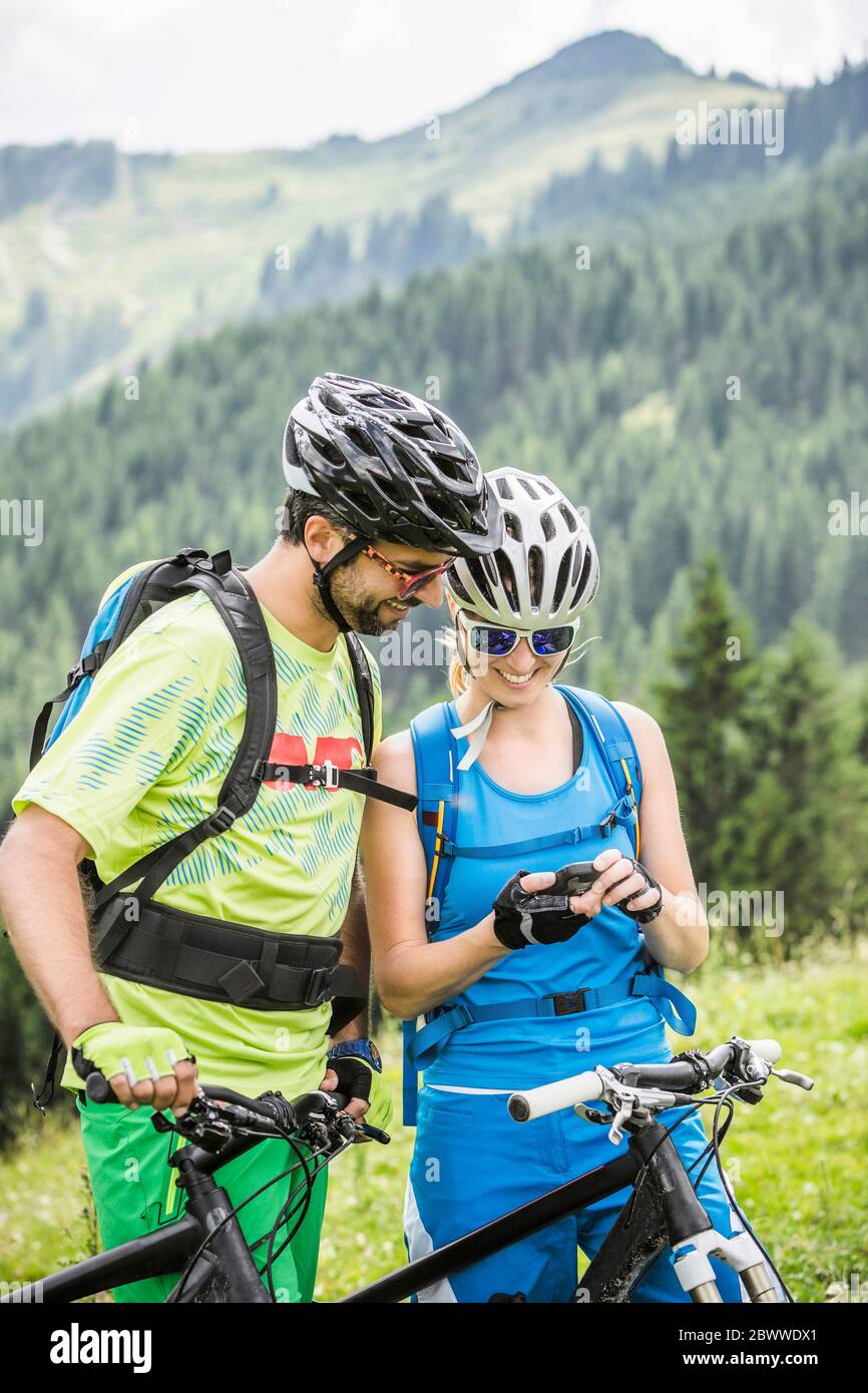 Couple with mountain bikes looking at mobile device in the mountains, Achenkirch, Austria Stock Photo