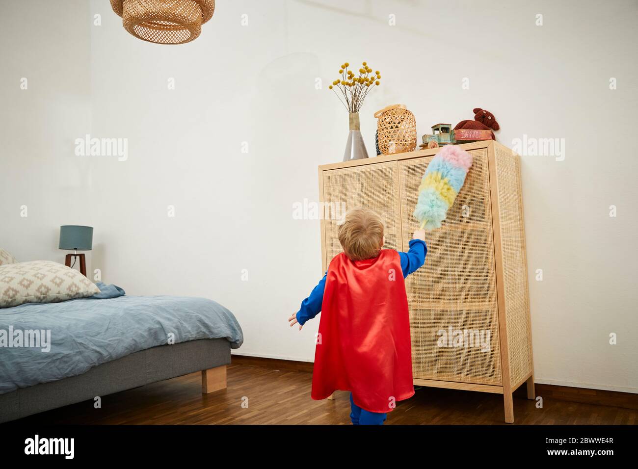 Boy wearing superman costume and cleaning with feather duster on a sideboard at home Stock Photo