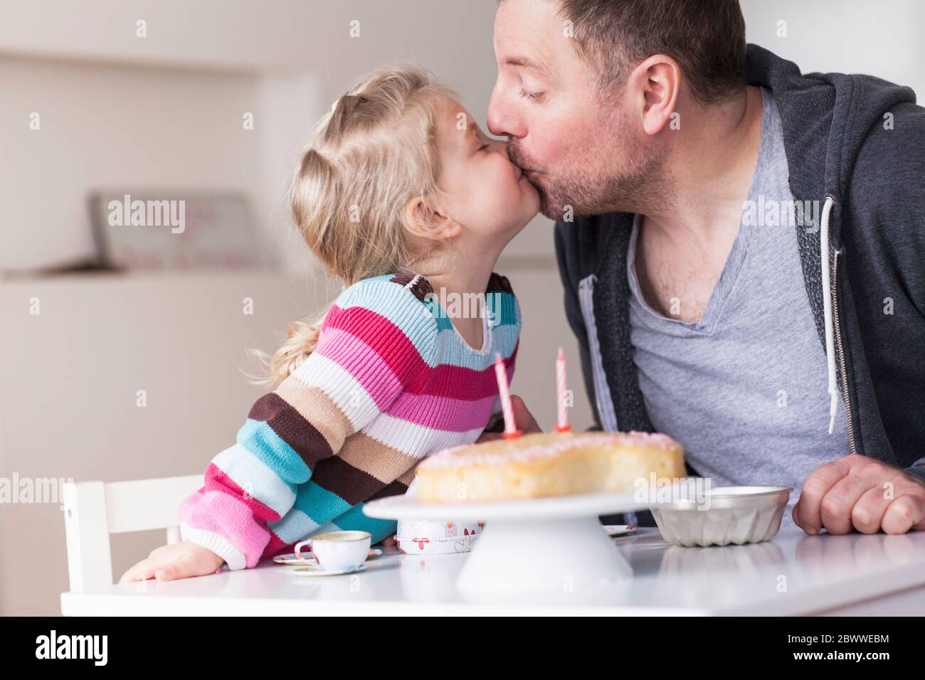 Father and daughter playing with doll's china set, kissing each other Stock Photo