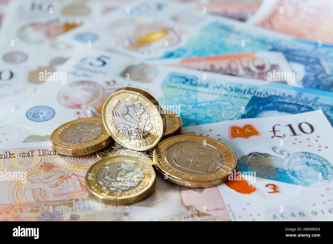 A pile of one pound £ coins British money sterling on new polymer £10 and £5 notes GBP close-up. England UK Britain Stock Photo