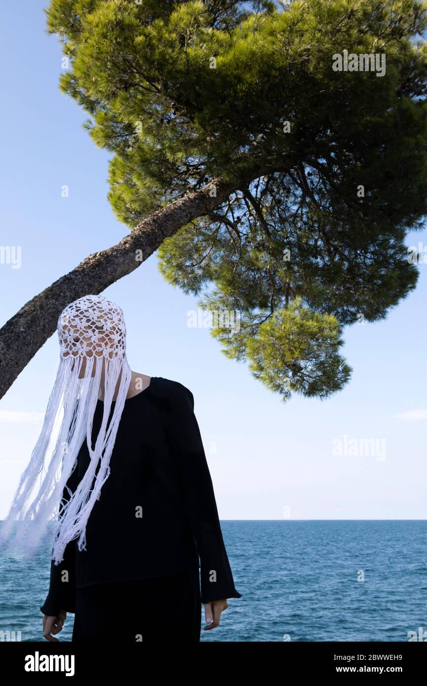Woman wearing crocheted white headdress with fringes standing in front of the sea Stock Photo