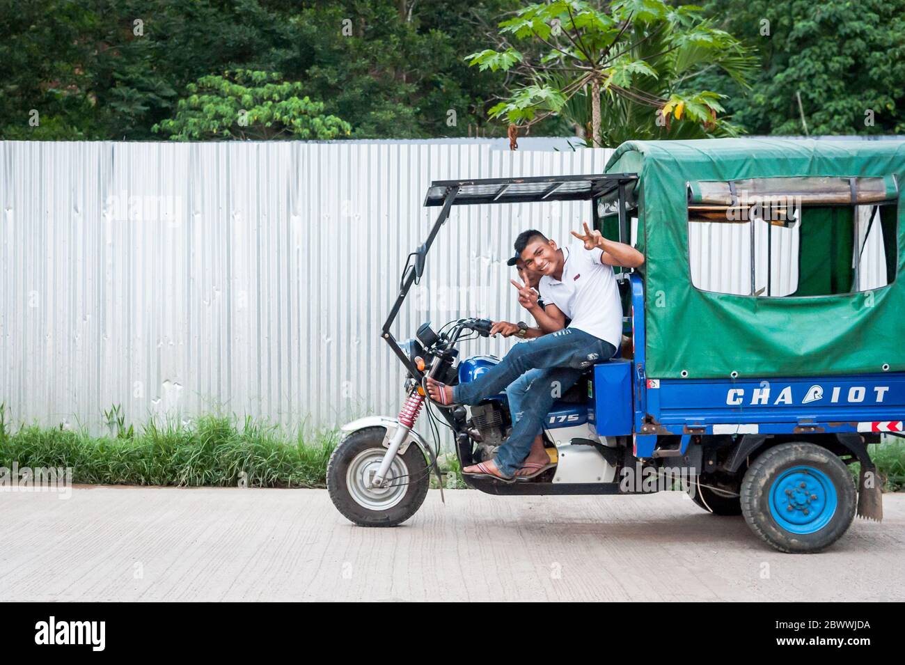 A filipino passenger jokes as he travels in a local delivery van powered by a motorbike on the island of Coron, Palawan, The Philippines. Stock Photo