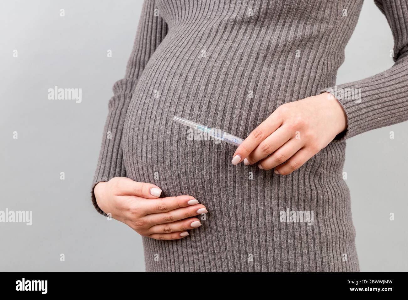 Close up of syringe for injection in pregnant woman's hand at colorful
