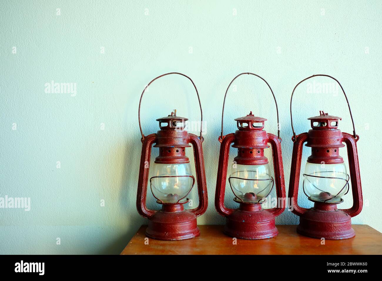 Vintage Red Paraffin Lamps on Wooden Table with White Concrete Wall Background. Stock Photo