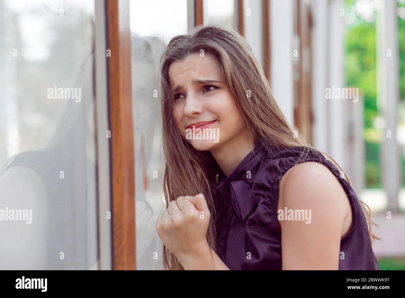 Upset outside in the city. Beautiful young woman with stressed about to cry near her office store window fist on glass crying. Negative human emotions Stock Photo