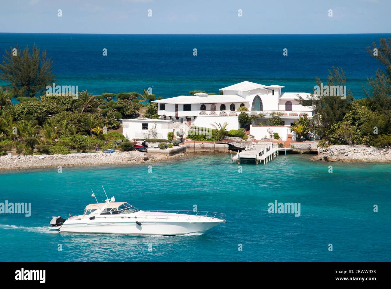 A white yacht passing by the residential house built on a narrow land