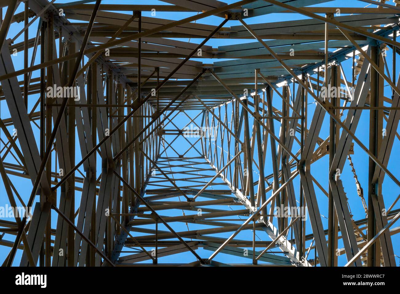 Looking up through the metal lattice of a high voltage electricity pylon against a blue sky Stock Photo