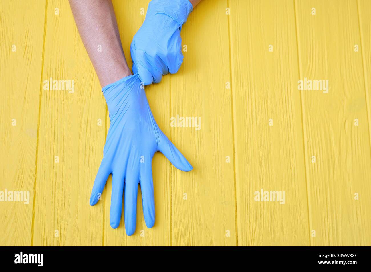 Blue Nitrile gloves. Hands of a medic in the blue latex gloves on a yellow wooden background with place for your text Stock Photo