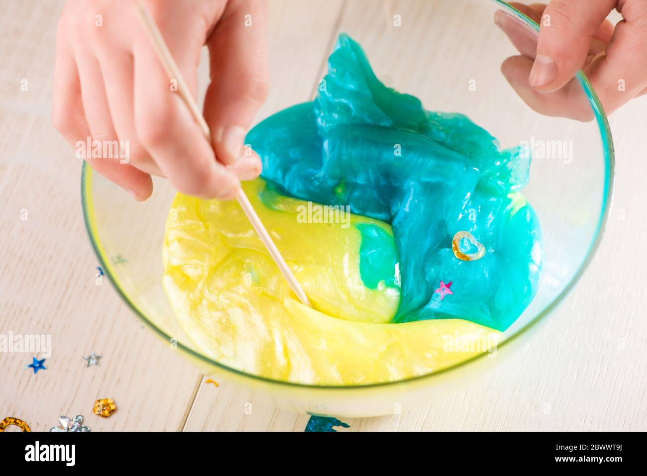 Girl mixing blue and yellow slime with shiny sequins in a bowl Stock