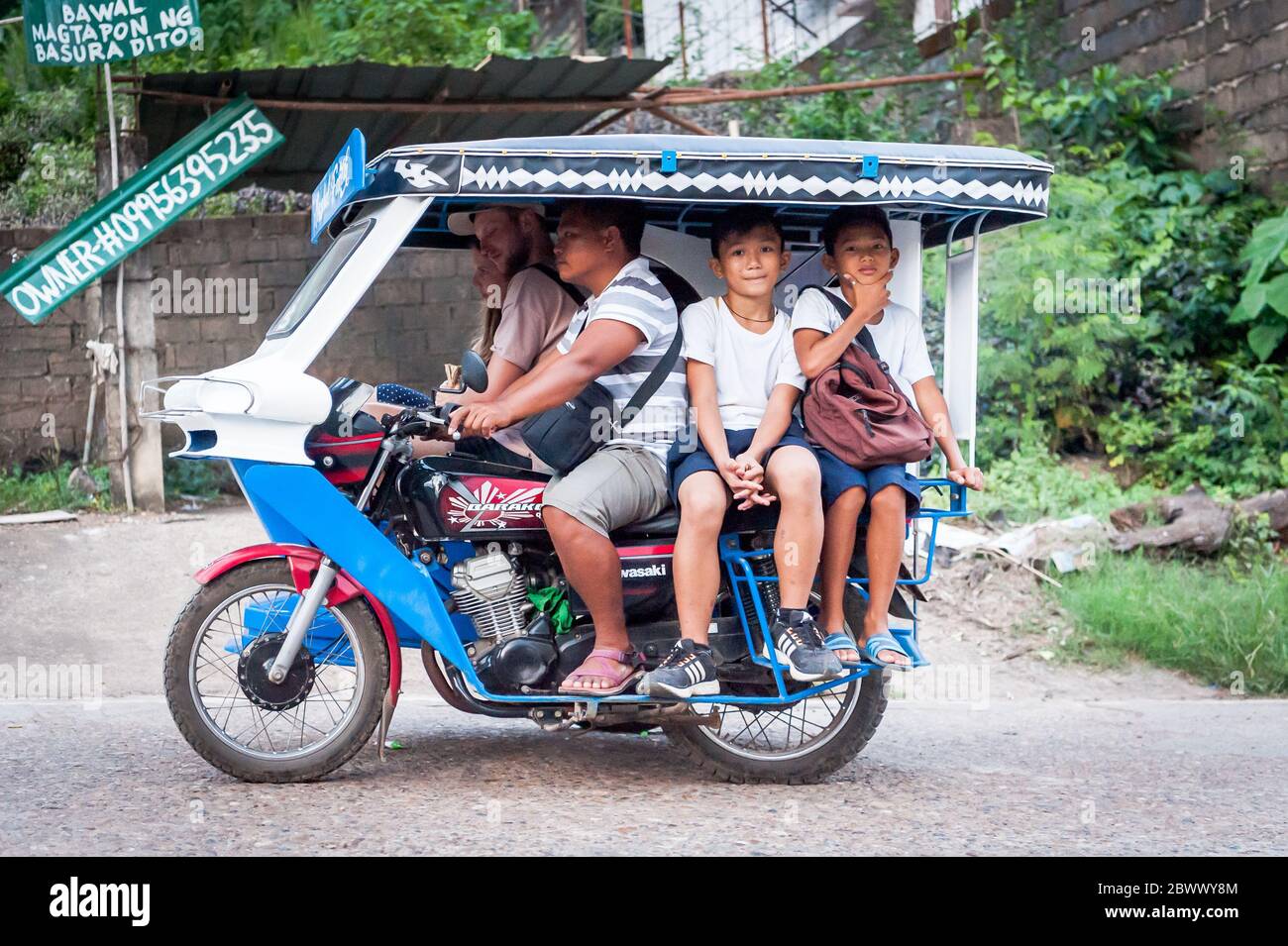 The famous filipino tricycle or tuk tuk (sometimes called rickshaw) makes its way along the busy main road going into Coron Town Proper. Coron Island. Stock Photo