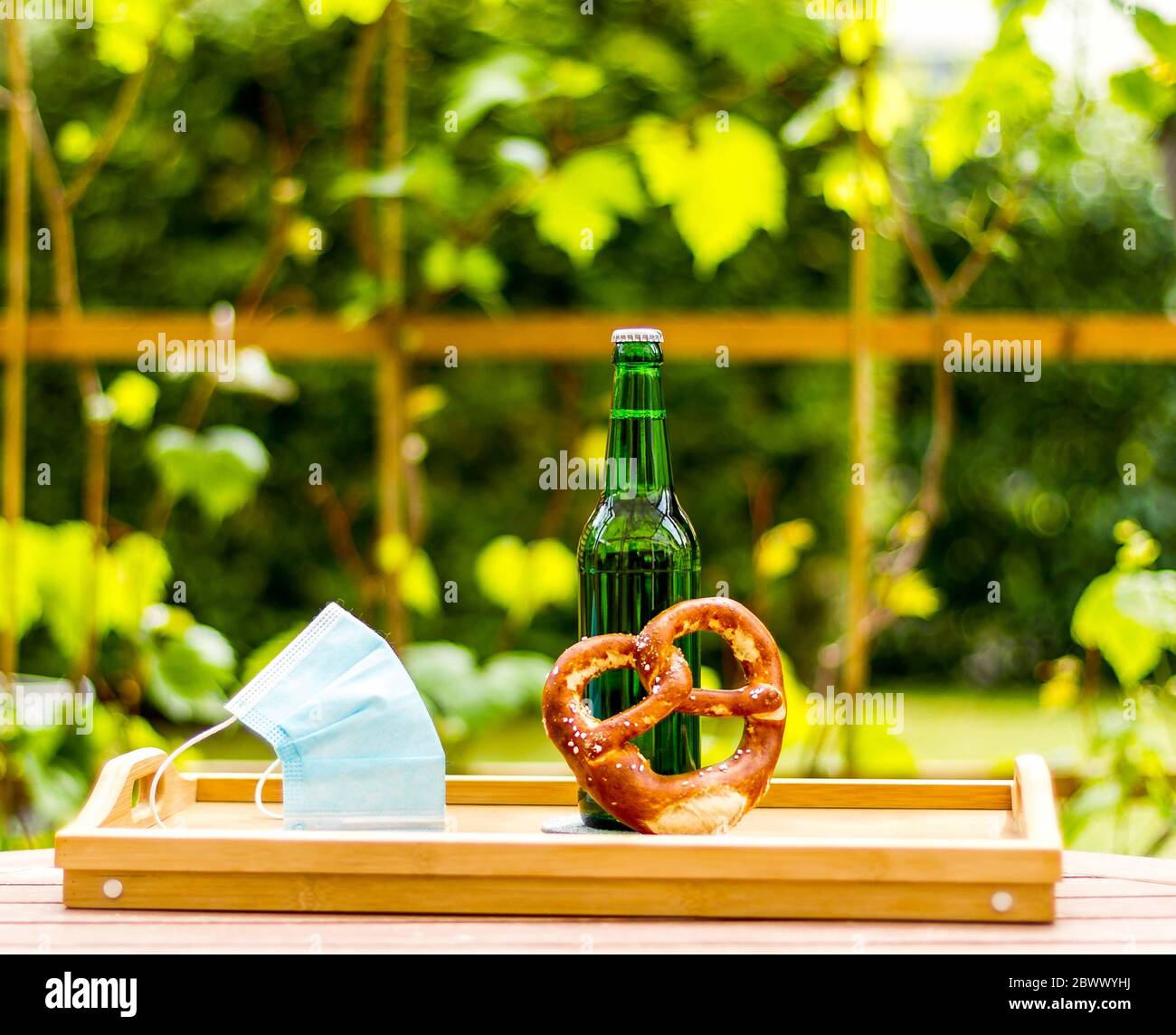 Green beer bottle with pretzel and face mask, bokeh effect Stock Photo