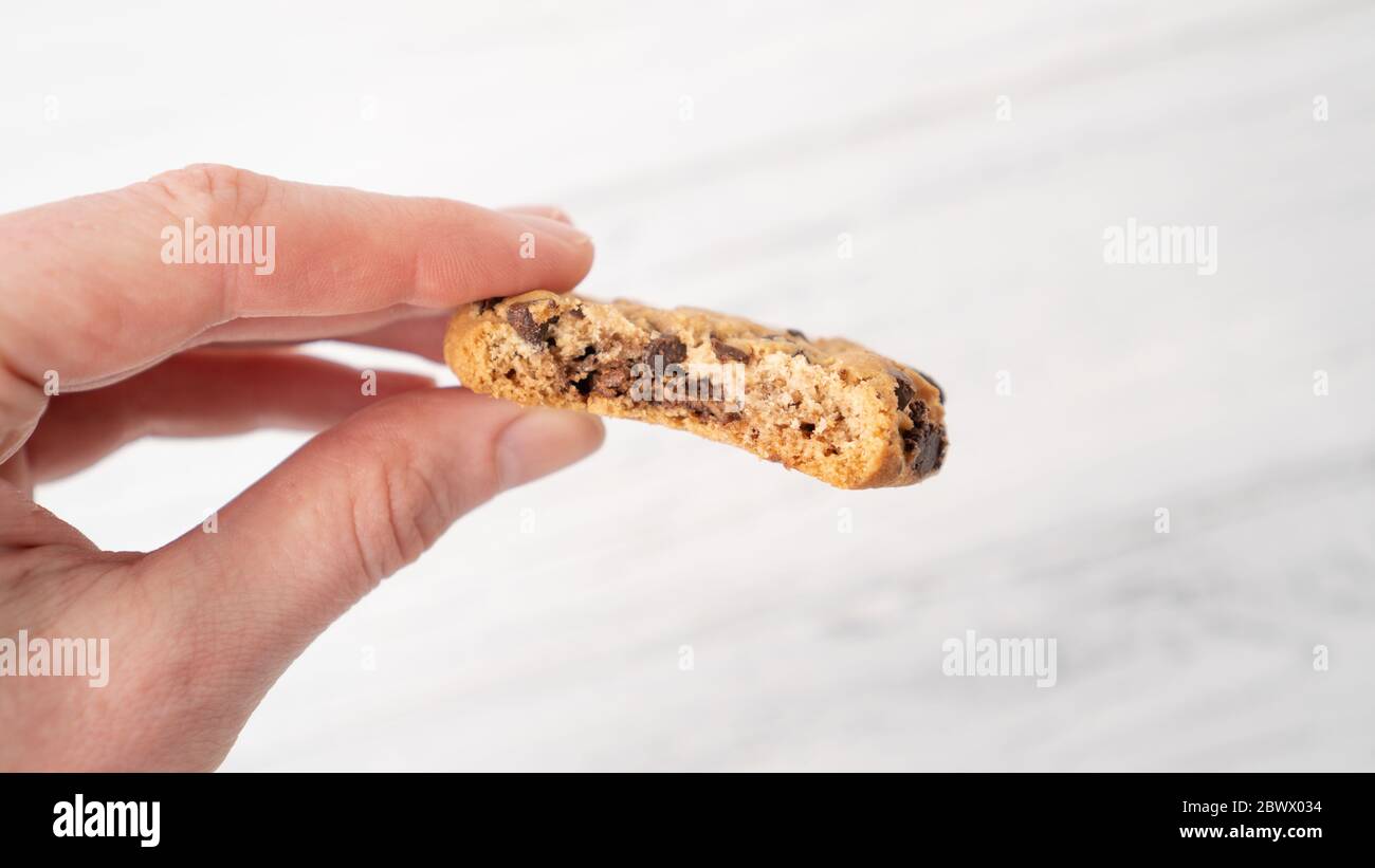 Bitten chocolate chip cookie in hand. Hand holding cookie with chocolate drops on white wooden background Stock Photo