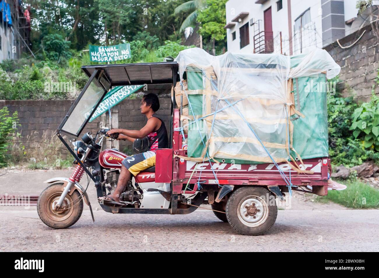 Motorbikes, trikes, lorries, cars and all manner of transport rushes through the dusty main road on Coron Island, Philippines at rush hour. Stock Photo