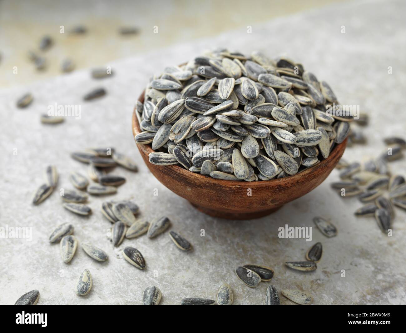 Sunflower seeds in terracotta bowl and scattered on stone surface Stock Photo