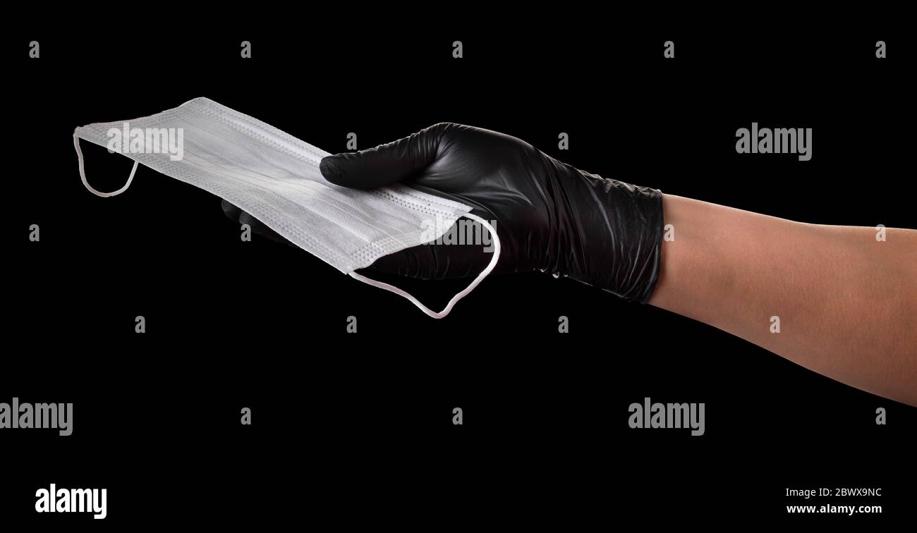 Hand in black gloves holding disposable face mask isolated on black ...